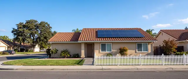 A single-story California home with solar panels on its tile roof under a clear blue sky